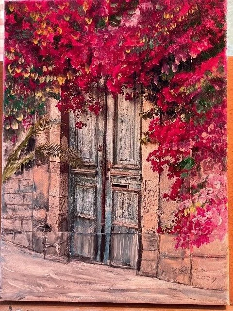 Weathered wooden door framed by vibrant red bougainvillea blooms, set against a stone wall, evoking a sense of charm and tranquility.